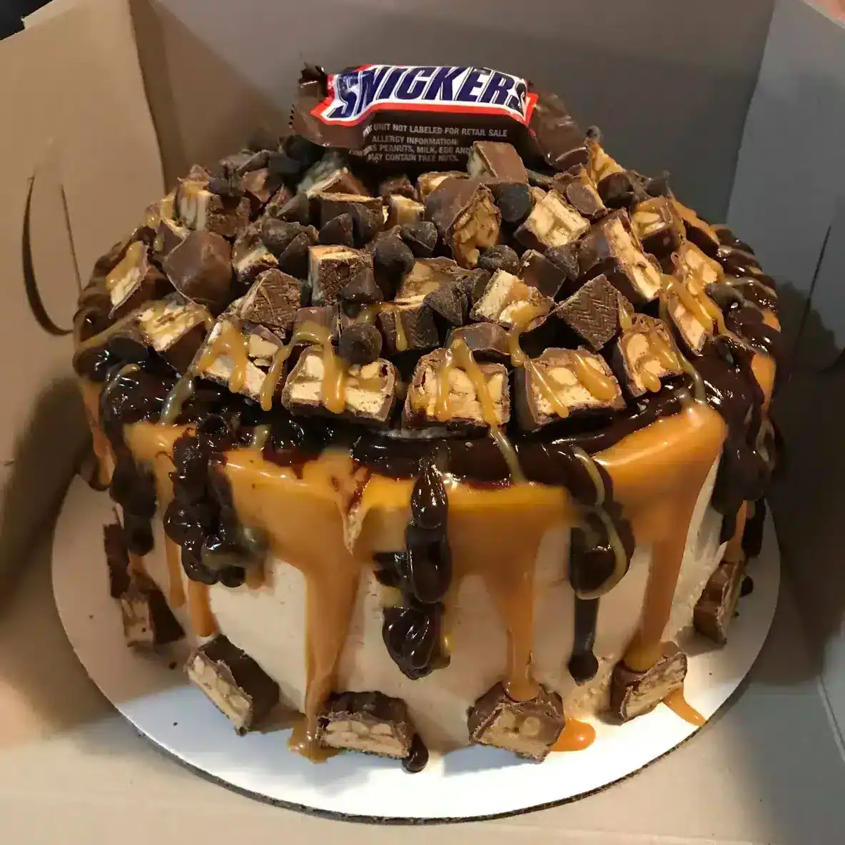 Rich Snickers-themed cake topped with chocolate, caramel, and chopped Snickers bars, perfect for special occasions and sweet cravings.