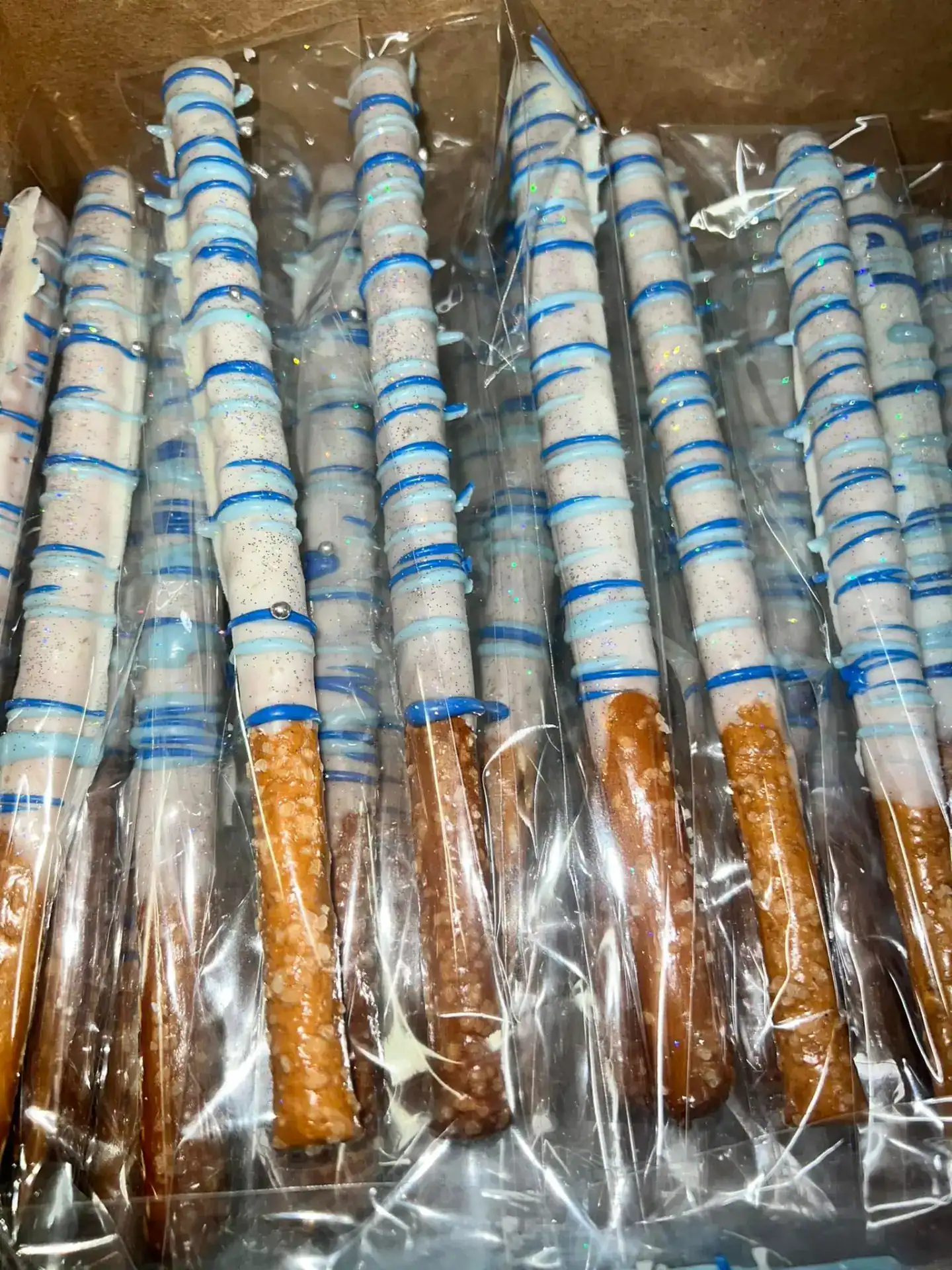 Delicious chocolate-covered pretzel rods decorated with white and blue icing, perfect for celebrations or as a tasty snack.